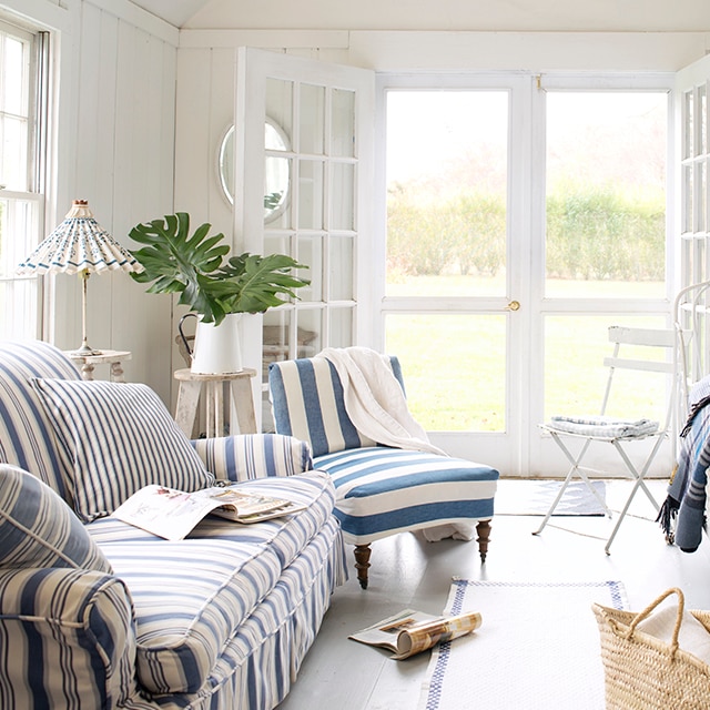 This bright, white-painted cottage living room has a relaxed, coastal vibe with blue and white stripe and slip-covered furniture, a vaulted ceiling, open French doors and screen doors. This bright, white-painted cottage living room has a relaxed, coastal vibe with blue and white stripe and slip-covered furniture, a vaulted ceiling, open French doors and screen doors.