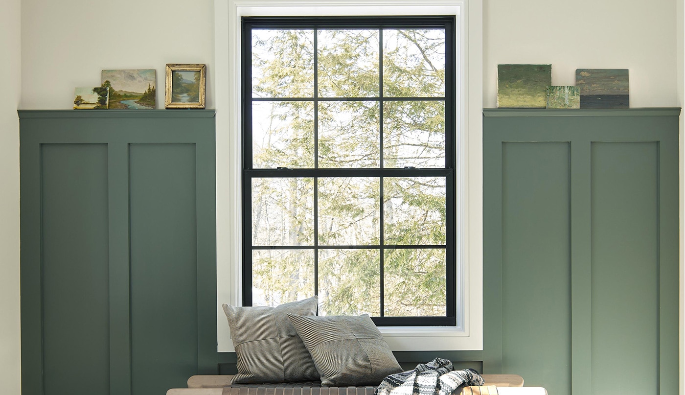 An inviting entryway with dark green-painted wainscoting, white walls and trim, a large window, and a bench with a throw and pillows.