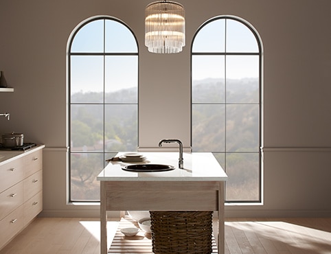 A kitchen with beige walls, two large arch windows, and an island with a sink. A kitchen with beige walls, two large arch windows, and an island with a sink.