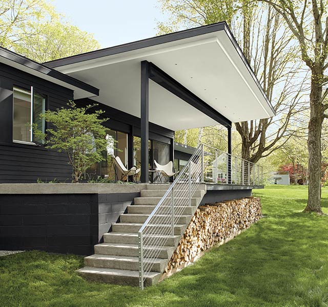 A modern style home with black painted exterior siding, and stairs leading to a porch with a white ceiling and black posts. A modern style home with black painted exterior siding, and stairs leading to a porch with a white ceiling and black posts.