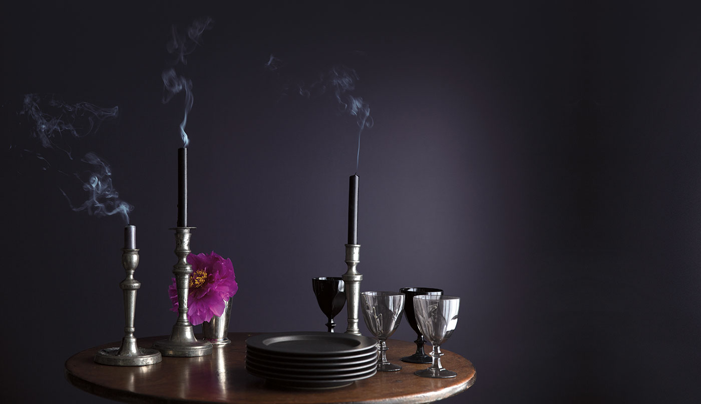 A wooden table with glasses, dishes, and candles in front of a dark purple wall.