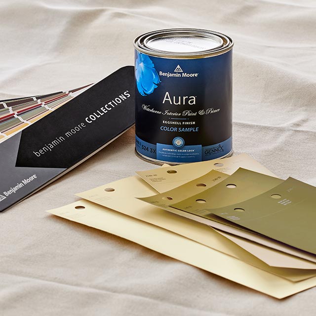 A color sample of Aura paint sitting on top of a tarp with a collections fan deck and neutral color swatches. A color sample of Aura paint sitting on top of a tarp with a collections fan deck and neutral color swatches.