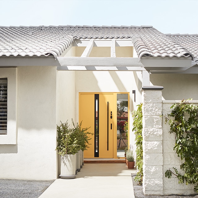 A sunny home exterior painted in off-white with a yellow front door, cacti and other desert landscaping. A sunny home exterior painted in off-white with a yellow front door, cacti and other desert landscaping.