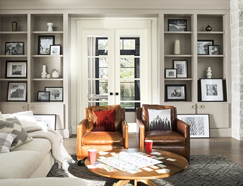 Salon confortable avec bibliothèques grises encastrées, portes-fenêtres blanches, sofa blanc et fauteuils en cuir brun. Salon confortable avec bibliothèques grises encastrées, portes-fenêtres blanches, sofa blanc et fauteuils en cuir brun.